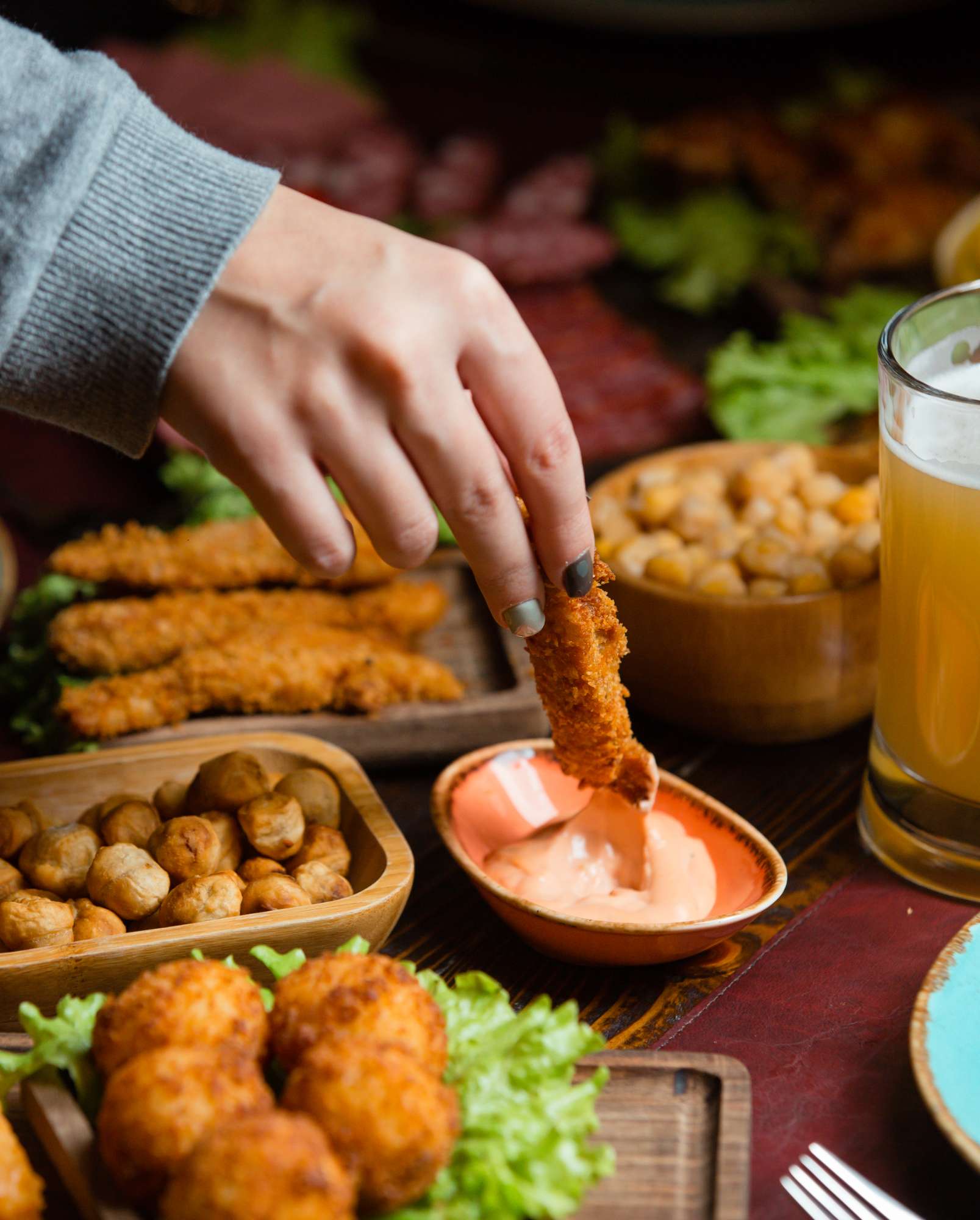 woman-dipping-chicken-croquette-into-sauce-beer-setup-with-nuts.jpg