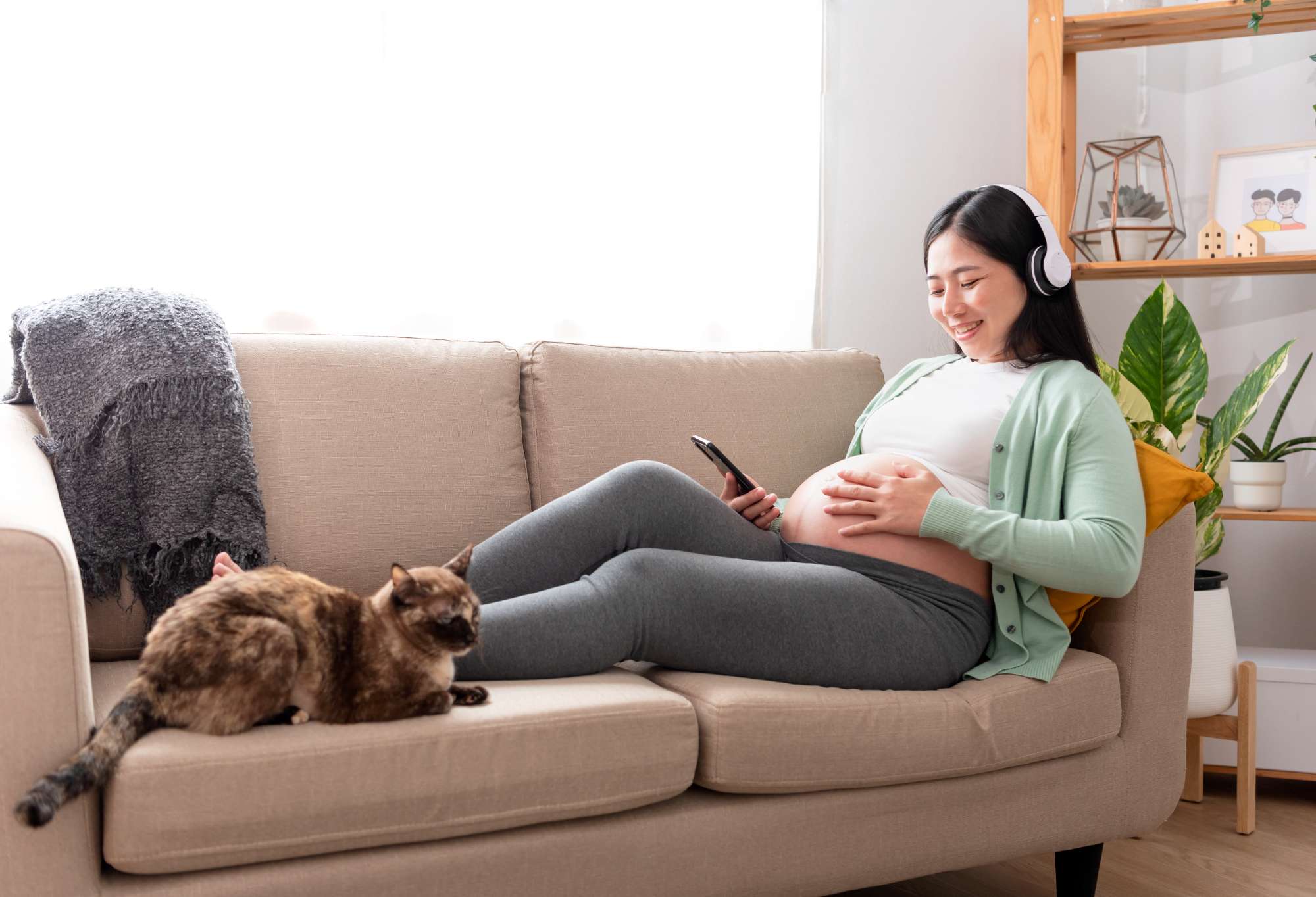 asian-beautiful-pregnant-woman-hands-fondle-belly-listening-music-with-headphones-sitting-sofa-home-pregnancy-maternity-preparation-expectation-concept.jpg