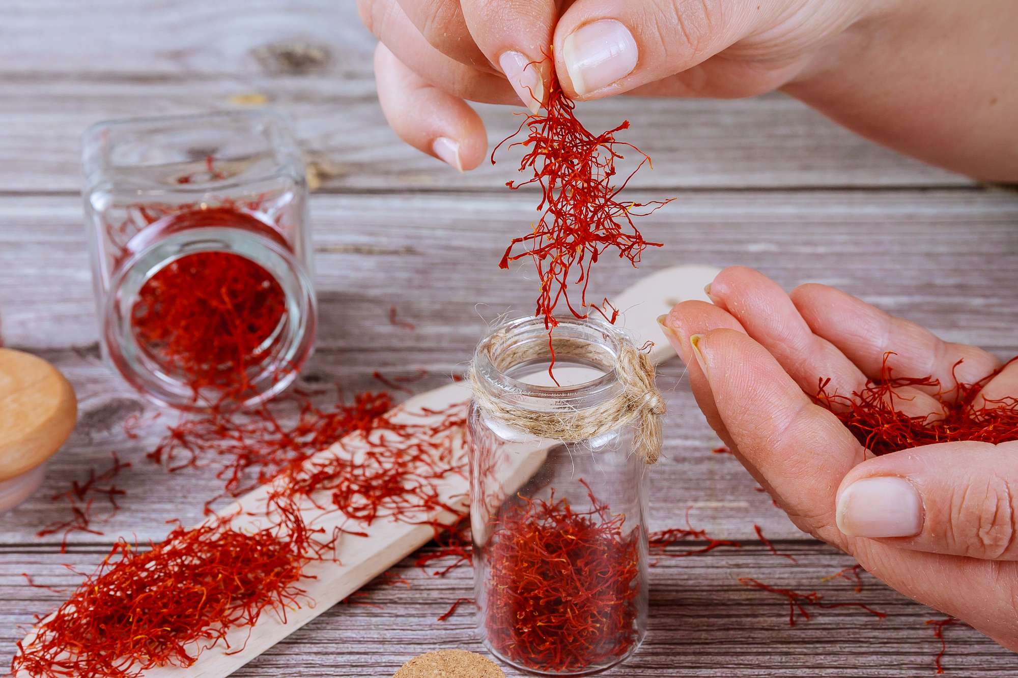 girl-puts-saffron-glass-container-saffron-spice-glass-bottle-wooden-spoon-wooden-background.jpg