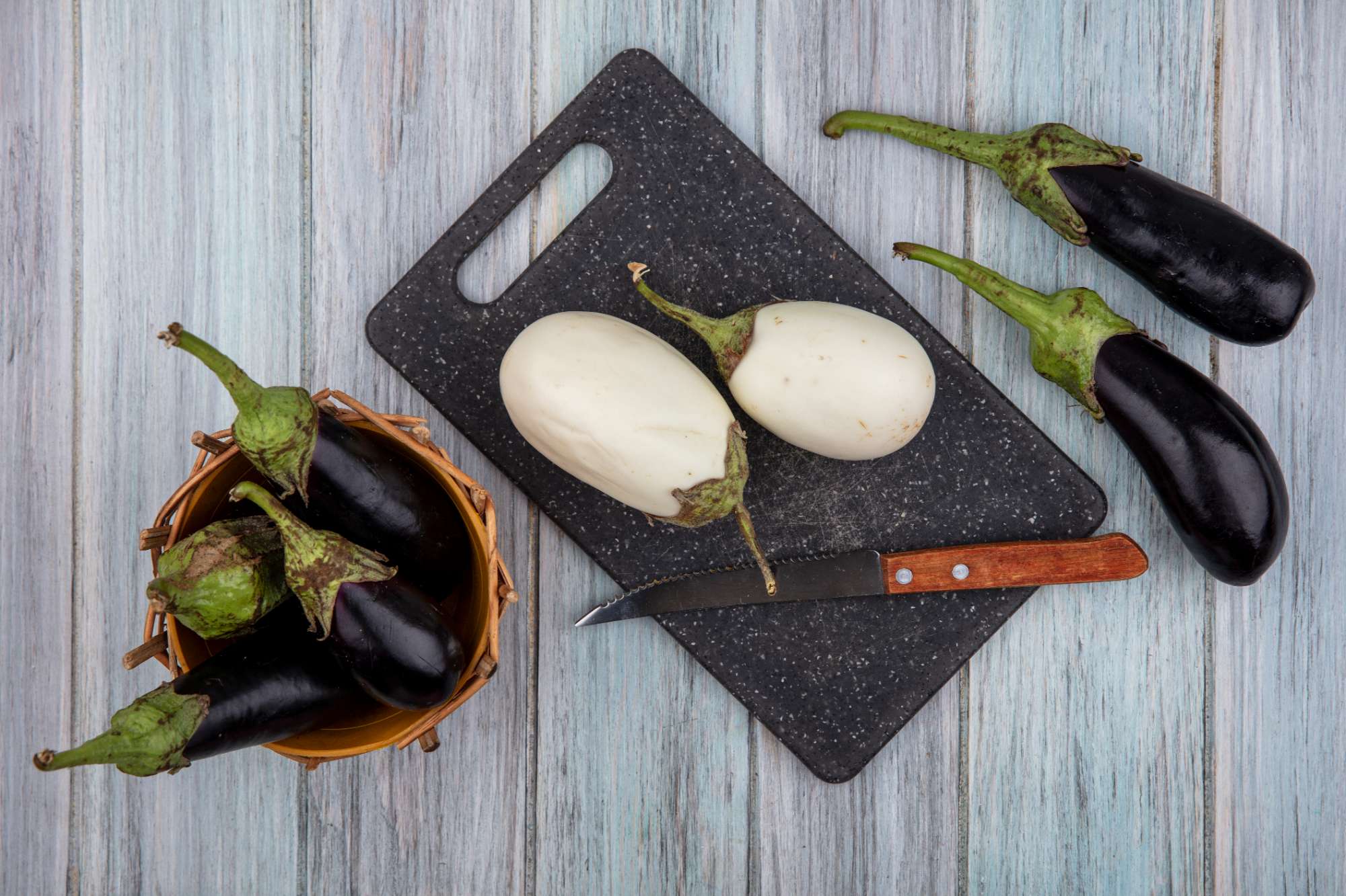 top-view-white-eggplants-knife-cutting-board-with-black-nadia-ones-basket-wooden-background.jpg