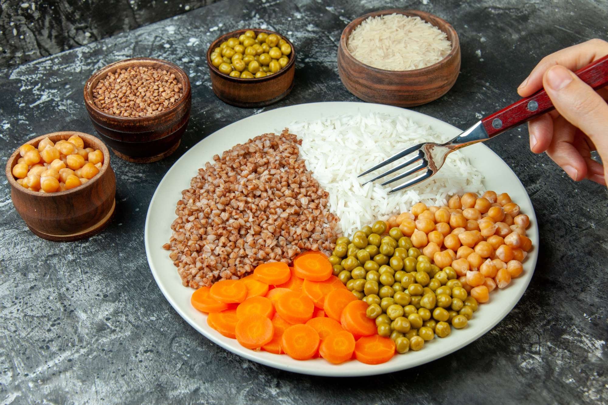 top-view-hand-holding-fork-delicious-vegan-meal-with-carrot-pisum-pea-buckwheat-rice-dark-color-background.jpg